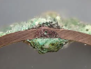 A photo of a pin-hole in a copper piping system, visible with a digital microscope, which demonstrates that the interior corrosion has propagated to the exterior, producing leaks. 
