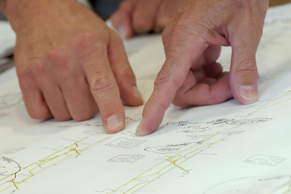 Close-up of engineers' hands pointing to technical plumbing and mechanical blueprints during a project consultation.
