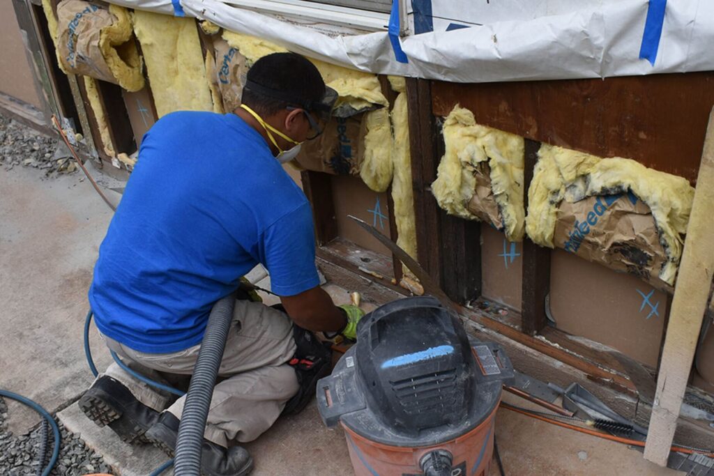 A worker in safety gear inspecting exposed wall studs and insulation during a construction defect remediation project.