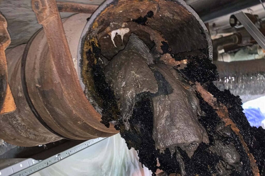 Interior view of a severely clogged and rusted cast iron drain pipe filled with dark sludge and debris.