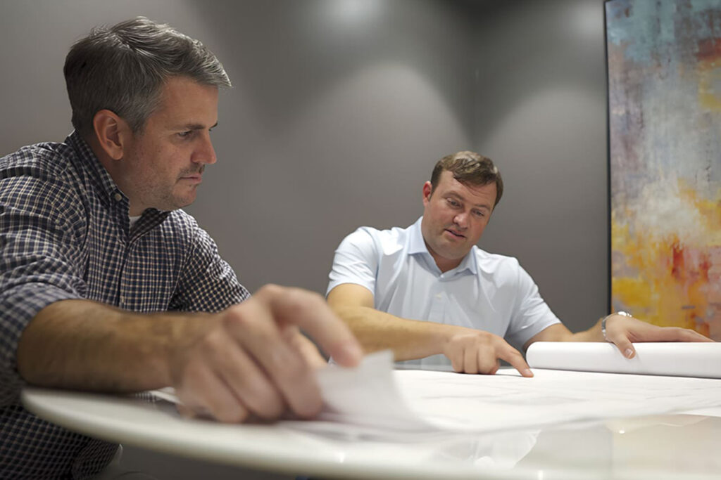 SageWater project managers discussing technical specifications while pointing to a large-scale plumbing schematic during a project planning meeting.