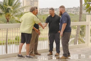 Four men shaking hands and smiling on an outdoor balcony overlooking a tropical landscape, representing a successful SageWater project completion.